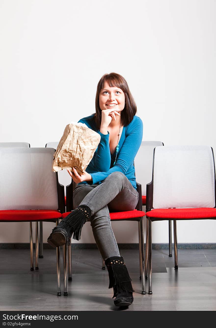 Happy smiling young woman sitting in cheer row, looking up, holding paper bag. Happy smiling young woman sitting in cheer row, looking up, holding paper bag