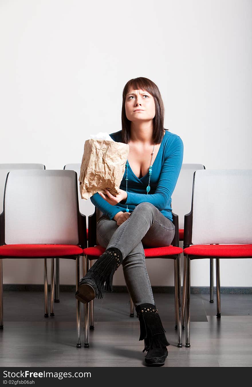 Worried young woman sitting with crossed legs in front cheer row, looking up, holding paper bag. Worried young woman sitting with crossed legs in front cheer row, looking up, holding paper bag