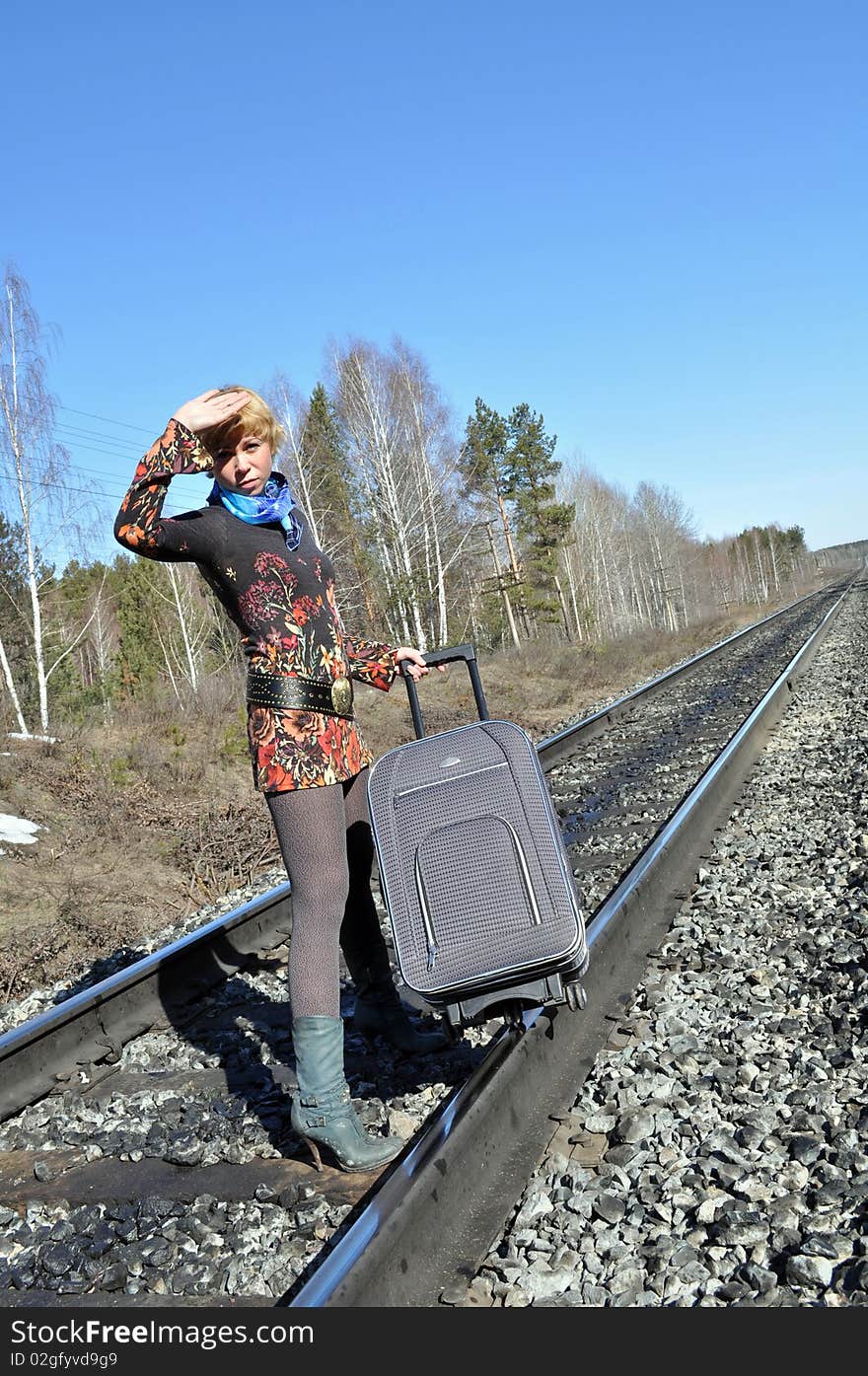 Young woman defends her hand face of the sun, with blonde hair and carries a bag on the tracks, the bright sun. Young woman defends her hand face of the sun, with blonde hair and carries a bag on the tracks, the bright sun