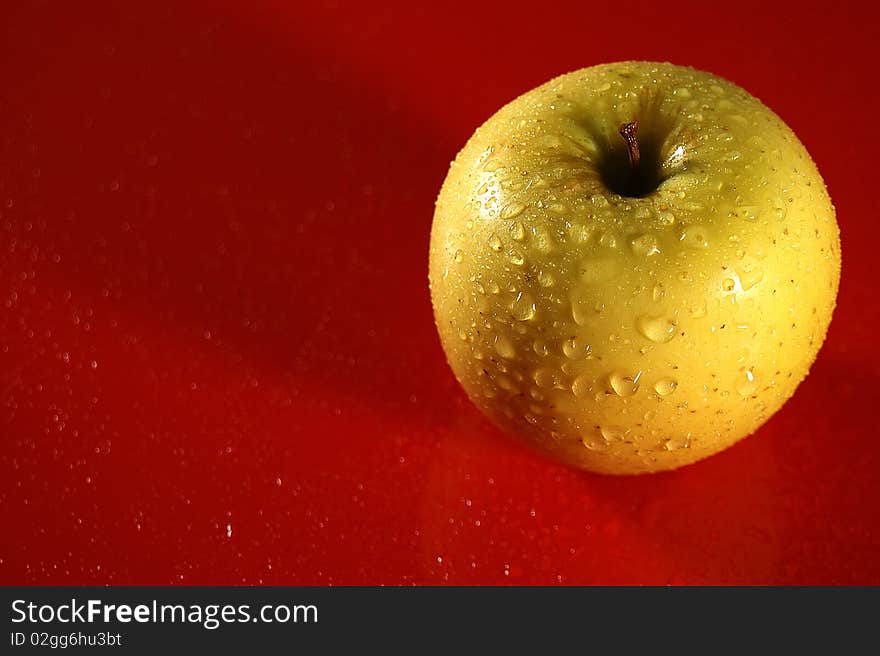 Yellow apple in drop of water on red background (overhand)