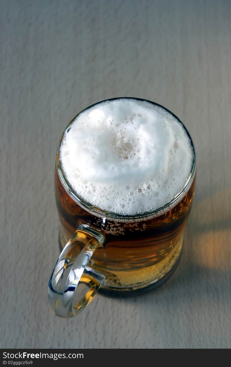 The full glass with foaming beer costs on a wooden table. The top point of shooting.