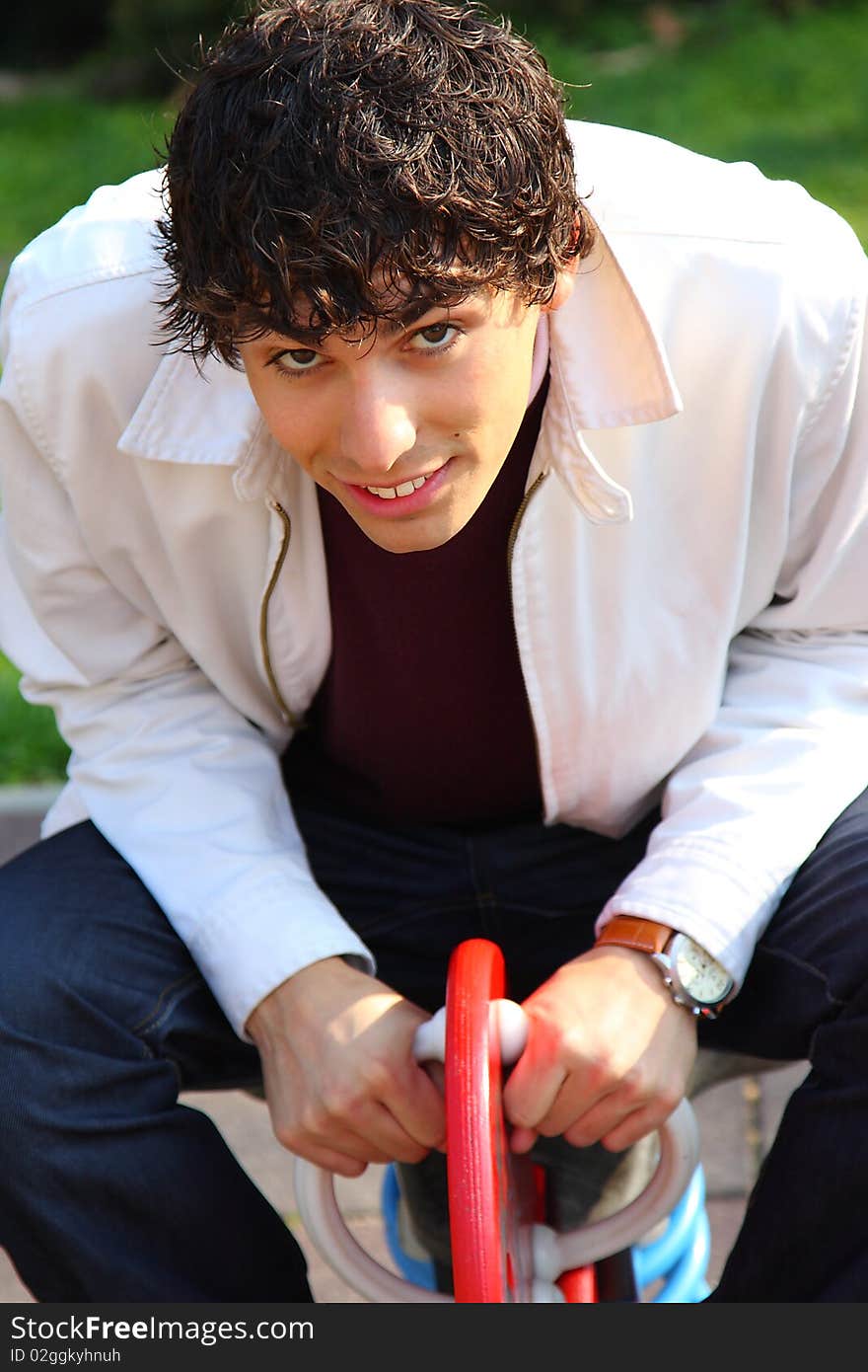 Curly haired young adult man in white, on a playground, outdoor portrait