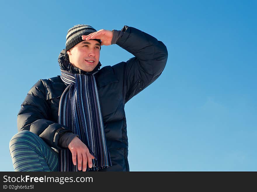 The young guy on a background of the sky looks in a distance in the winter