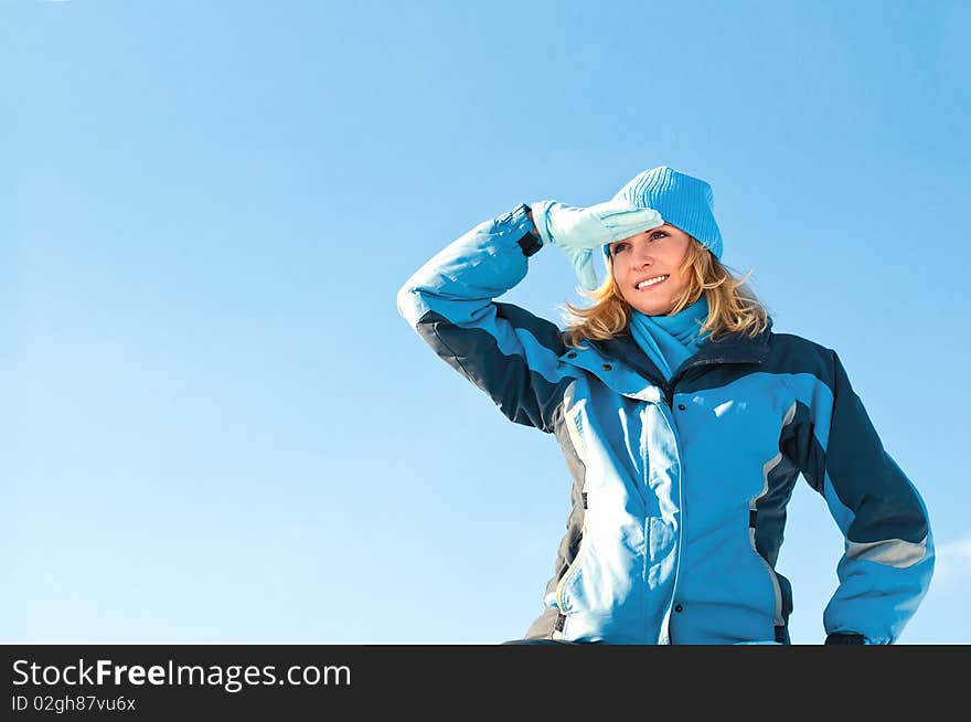 The young girl on a background of the sky looks in a distance in the winter