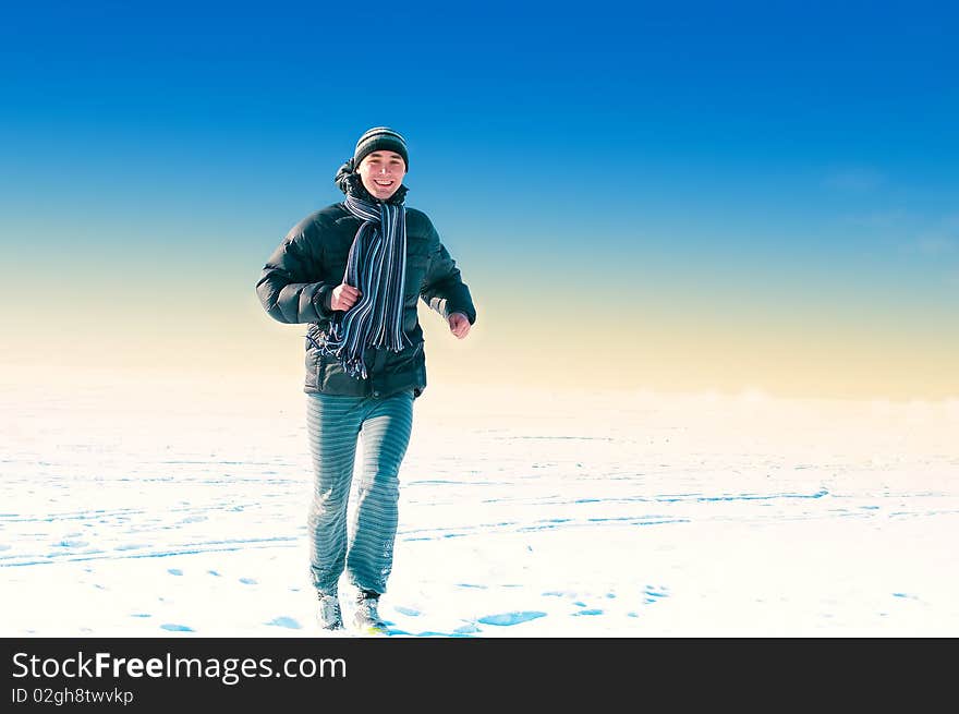 The young guy on a background of the sky looks in a distance in the winter