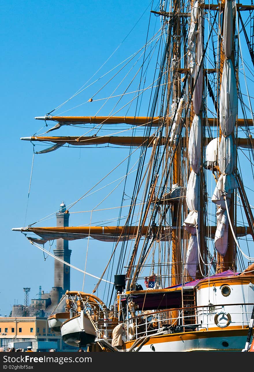 The impressive three masts of an old sailing ship moored in the port of Genoa and on the background the lighthouse symbol of the city