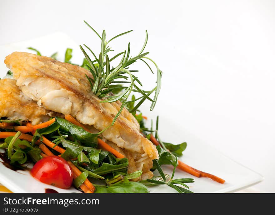 Pan seared fillet of white fish and vegetables on white background