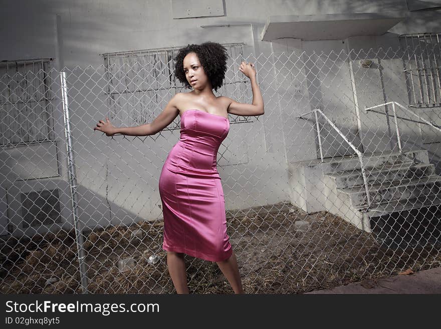 Young woman posing by an abandoned building with a surrounding fence. Young woman posing by an abandoned building with a surrounding fence