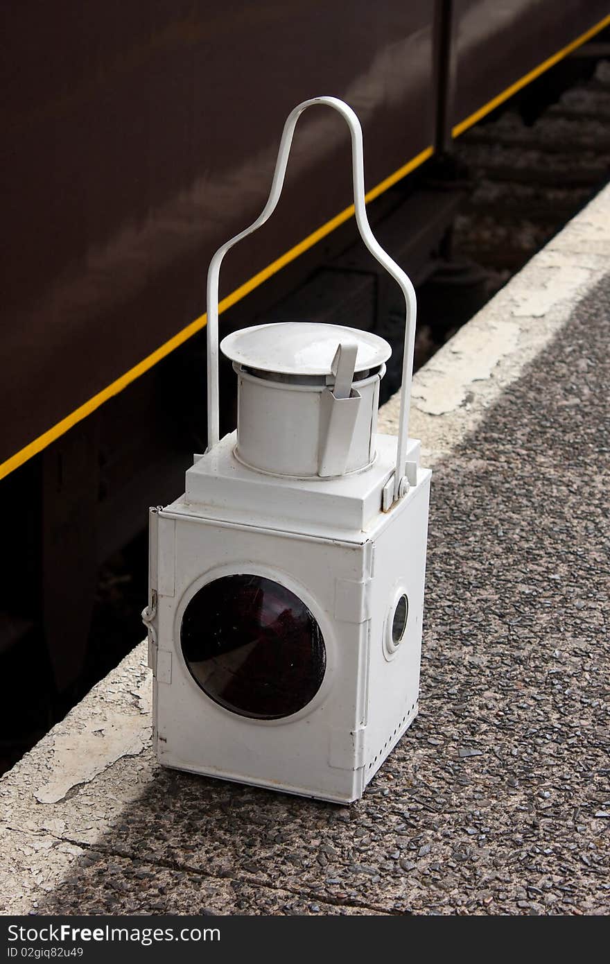 A White railway lamp with red lens resting on the platform