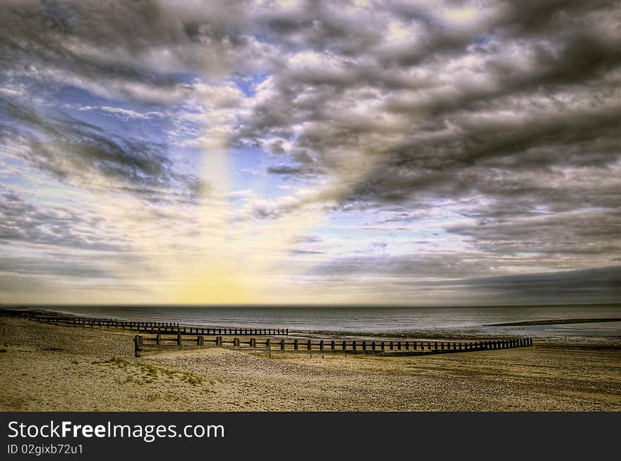 A deserted beach at sunset with a cloudy sky.