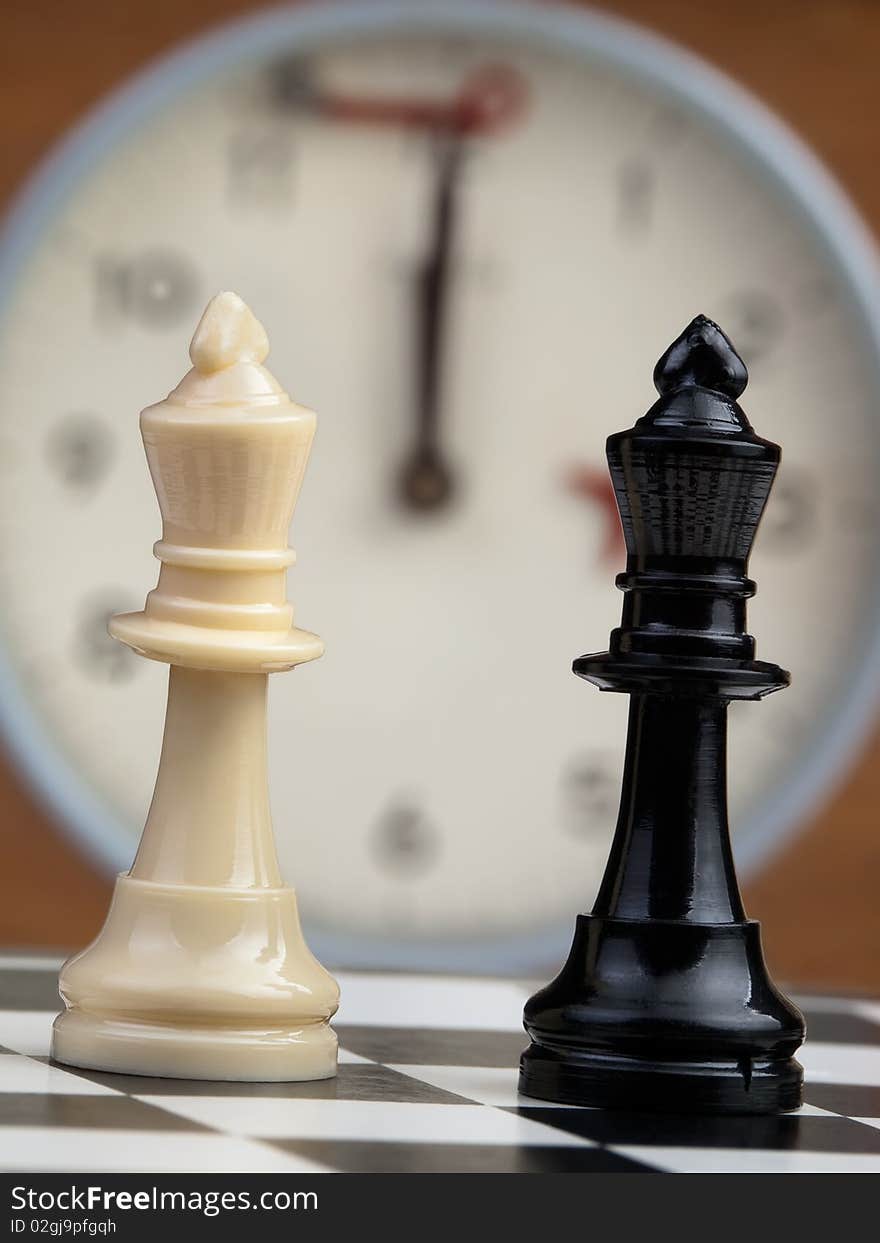 White and black king on the chessboard opposing each other,old chess clock in the background,can be used as concept for conflict,meeting,agreement. White and black king on the chessboard opposing each other,old chess clock in the background,can be used as concept for conflict,meeting,agreement..