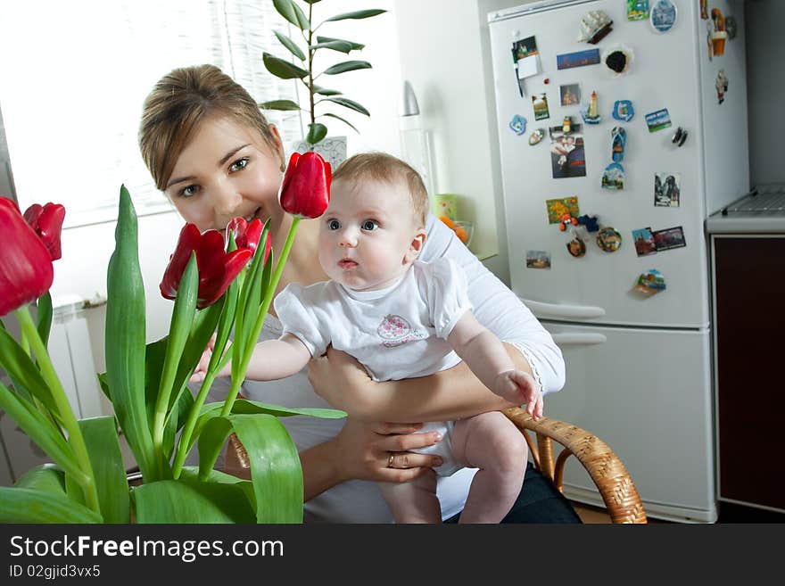 Young beautiful mother feeding her litlle cute baby daughter at the kitchen. Young beautiful mother feeding her litlle cute baby daughter at the kitchen