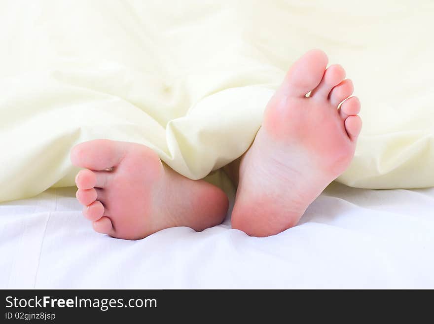 A couple of tiny feet poking out the end of the bed under the blanket. A couple of tiny feet poking out the end of the bed under the blanket