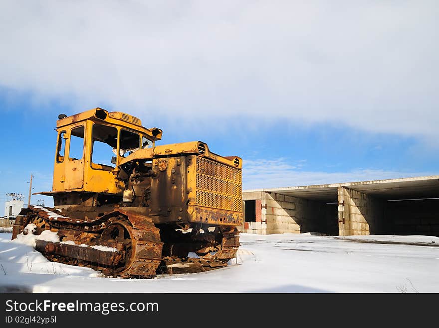 The thrown yellow tractor against the cloudy sky. Winter. The thrown yellow tractor against the cloudy sky. Winter