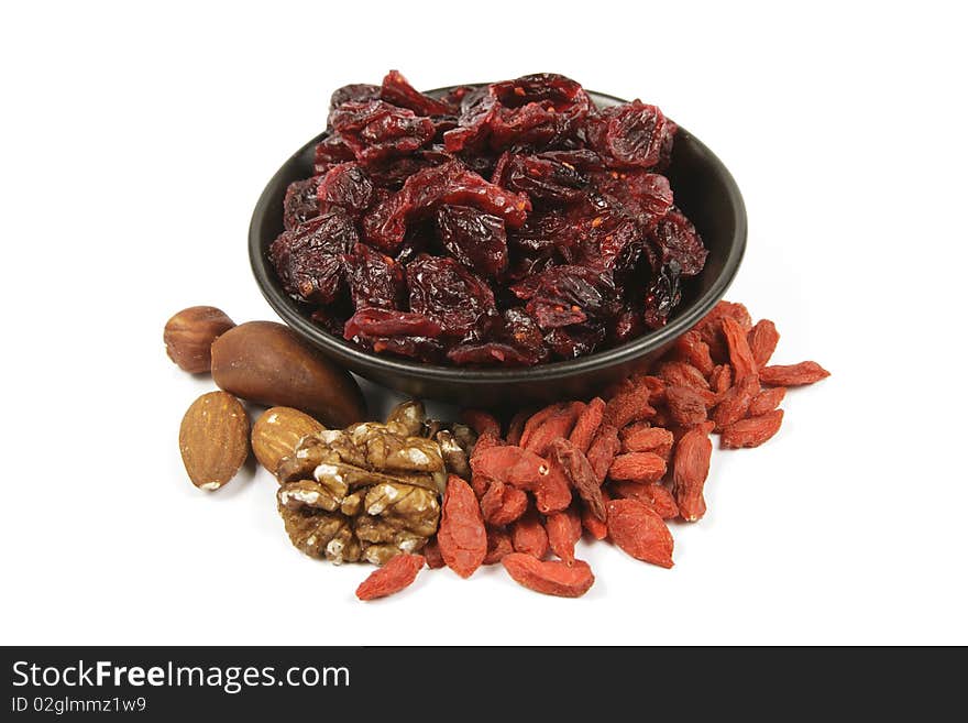 Red ripe dried cranberries in a small black bowl with mixed nuts and goji berries on a reflective white background. Red ripe dried cranberries in a small black bowl with mixed nuts and goji berries on a reflective white background