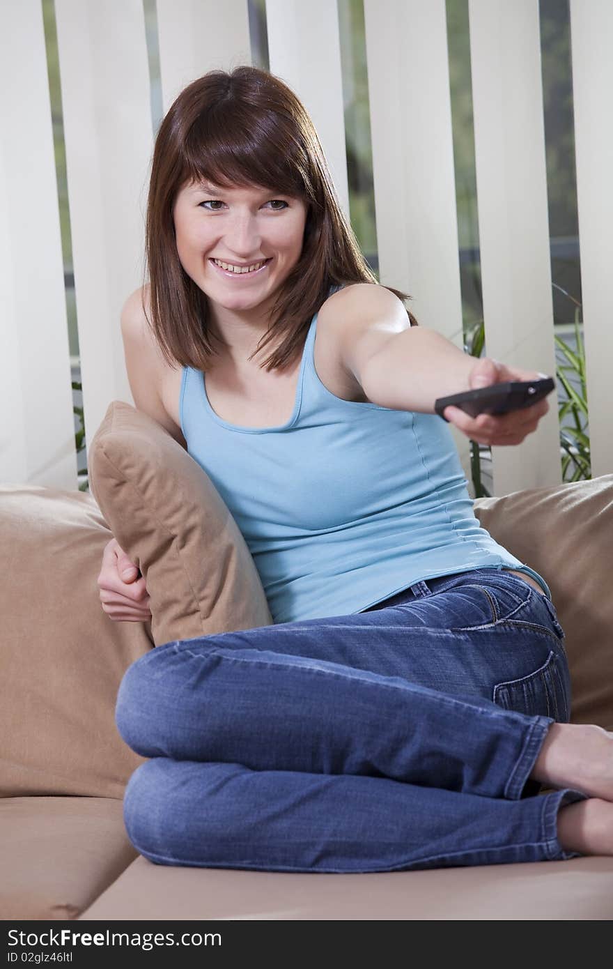 Young female in blue jeans sitting on the sofa and watching television. Young female in blue jeans sitting on the sofa and watching television