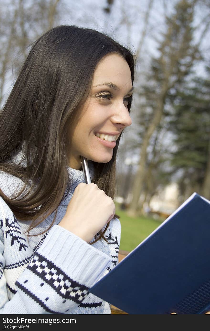 Young woman sunny day in the park thought. In the hands of a notebook with pen. Young woman sunny day in the park thought. In the hands of a notebook with pen