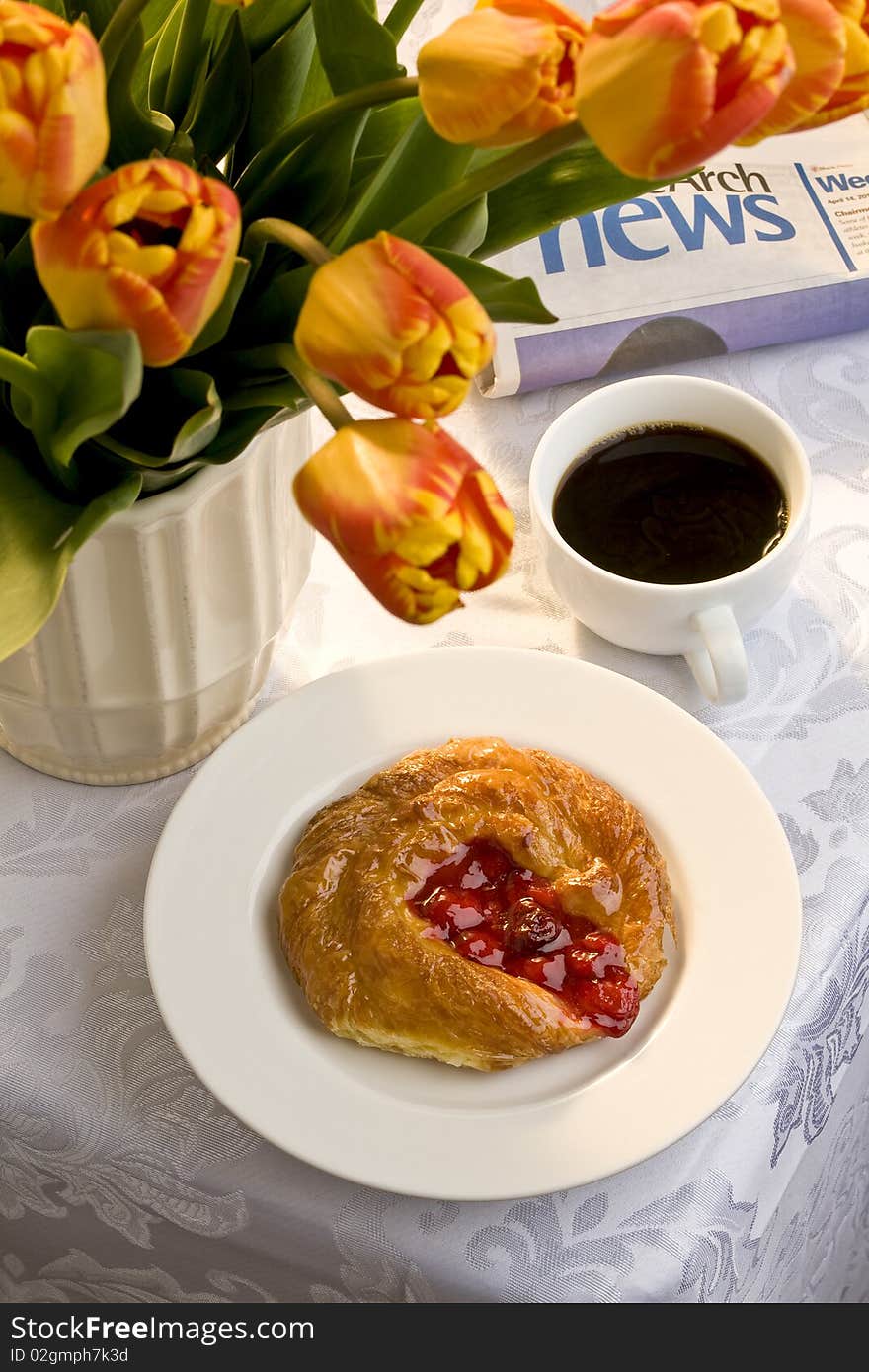 Cherry danish on a white plate with a cup of black coffee, a newspaper and a bunch of tulips. Cherry danish on a white plate with a cup of black coffee, a newspaper and a bunch of tulips