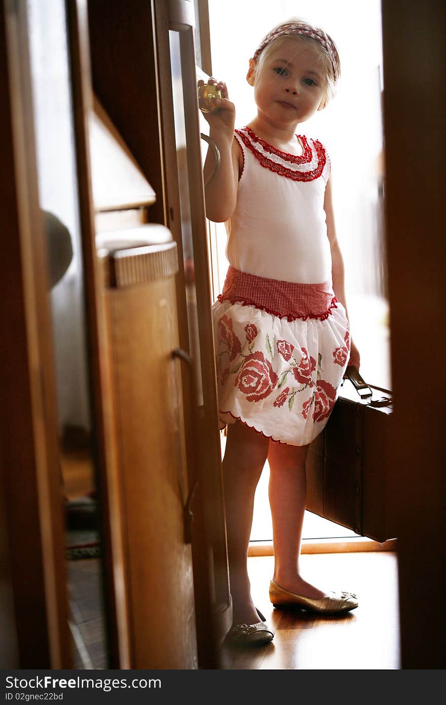 Little blonde girl waiting at front door ready to go on trip with suitcase in hand. Little blonde girl waiting at front door ready to go on trip with suitcase in hand.