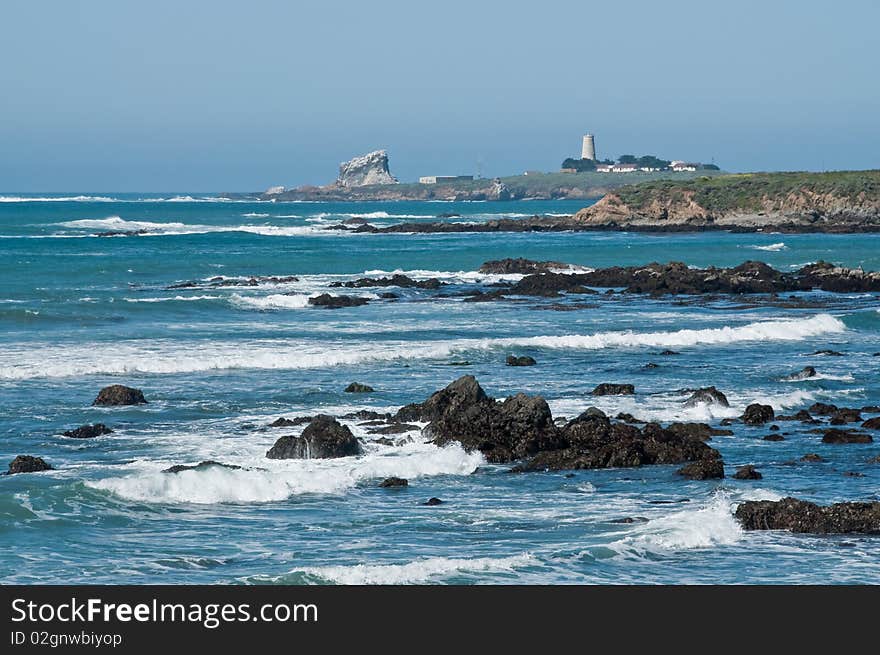 The rocky coastline of California with a lighthouse in the distance. The rocky coastline of California with a lighthouse in the distance