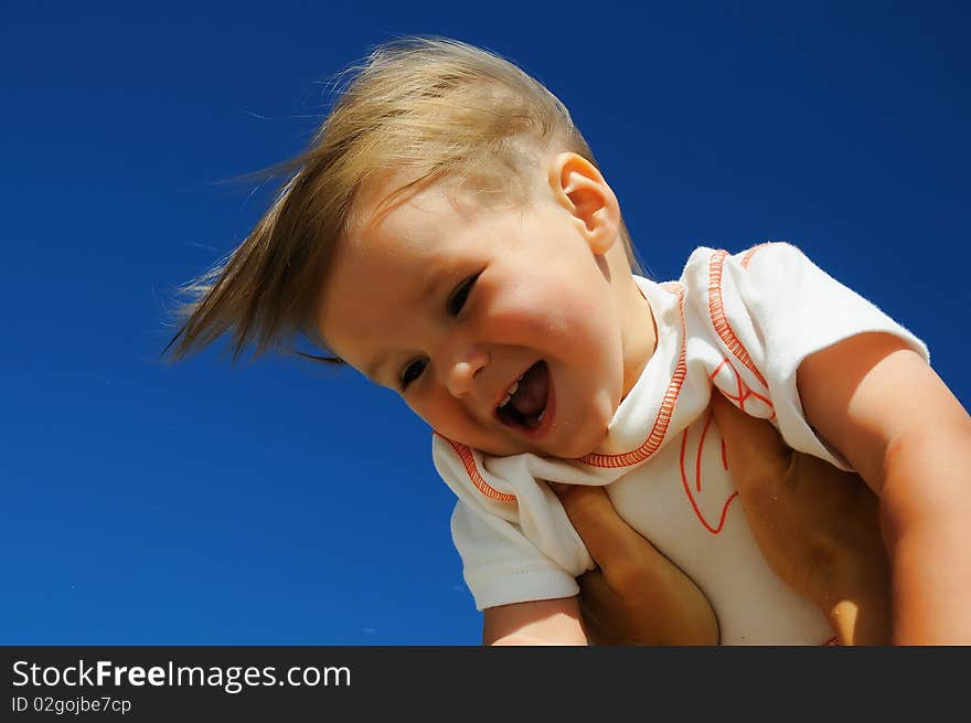 Charming little happy girl laughing in the arms of his mother, against the blue sky