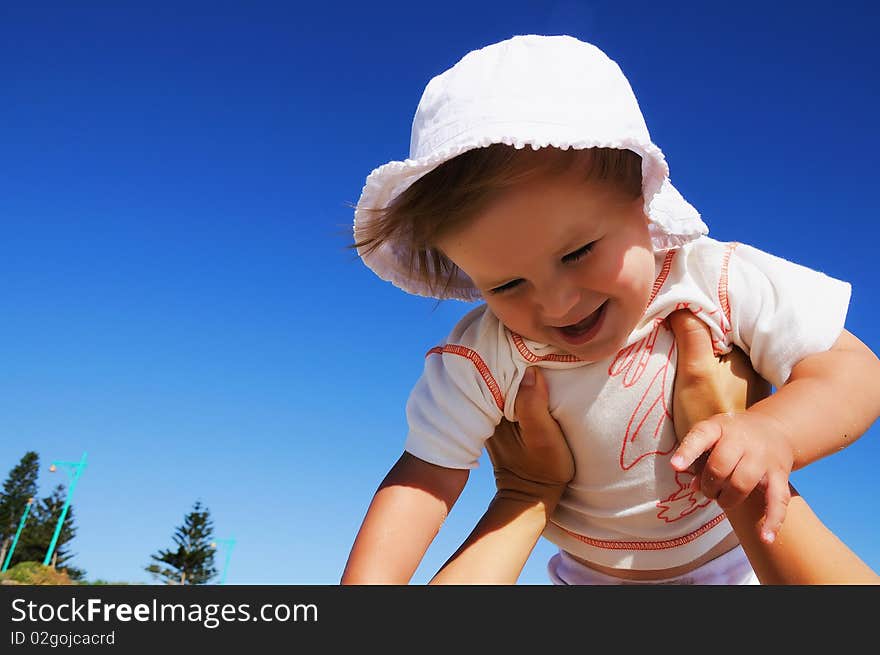 Charming little happy girl laughing in the arms of his mother, against the blue sky