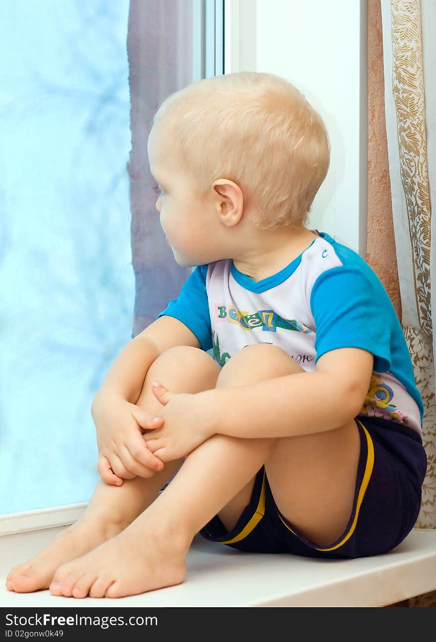 Boy sitting on the windowsill clutching her knees to her, and looks out the window. Boy sitting on the windowsill clutching her knees to her, and looks out the window