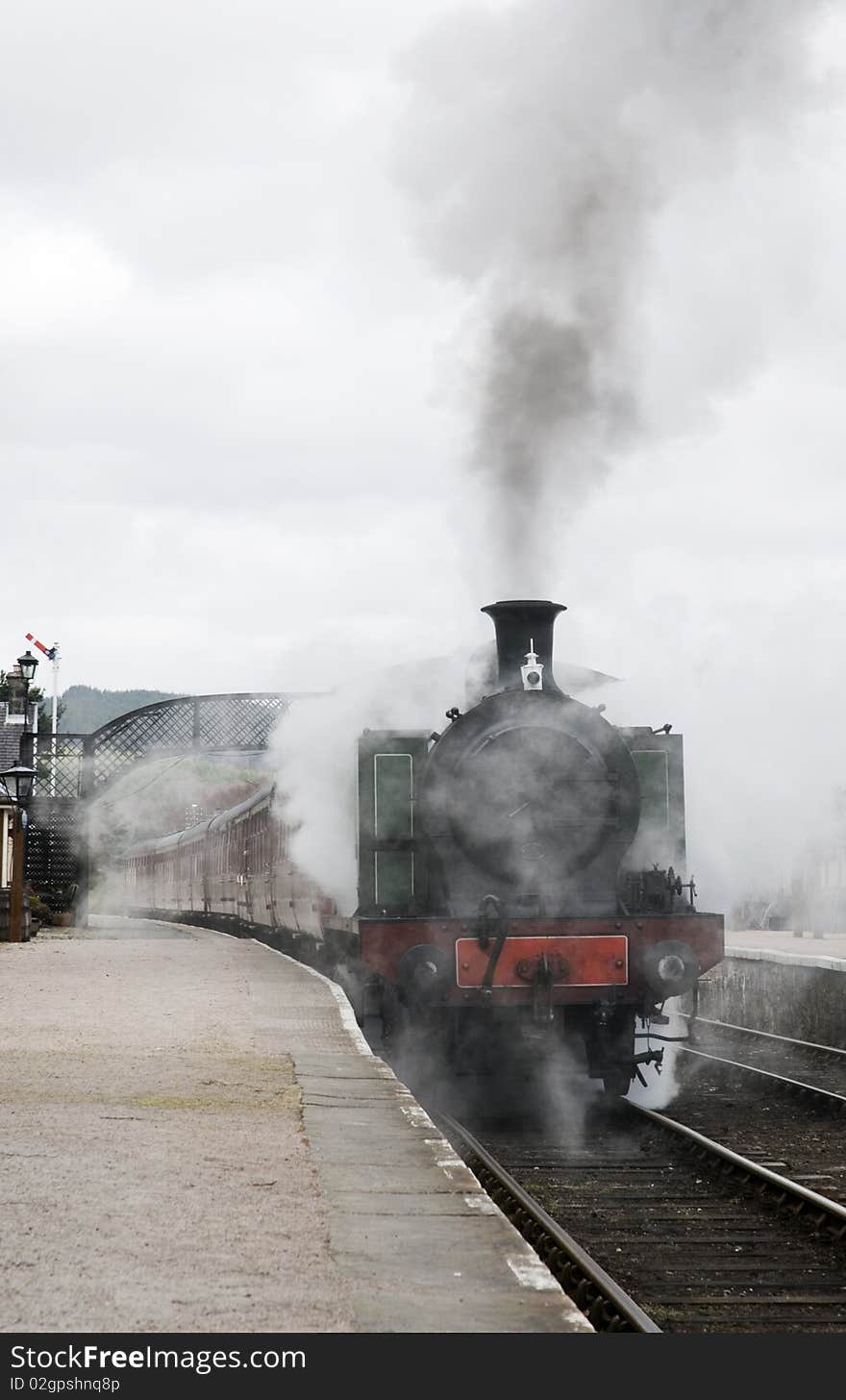 A vertical image of a steam locomotive leaving the station with lots of smoke and steam. A vertical image of a steam locomotive leaving the station with lots of smoke and steam