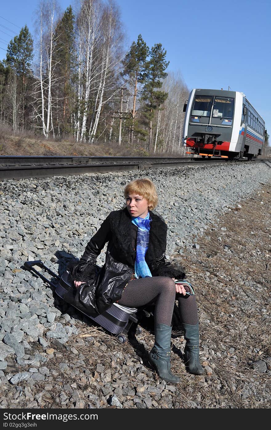 Woman sitting on a railway embankment, coming from behind a small locomotive. Woman sitting on a railway embankment, coming from behind a small locomotive