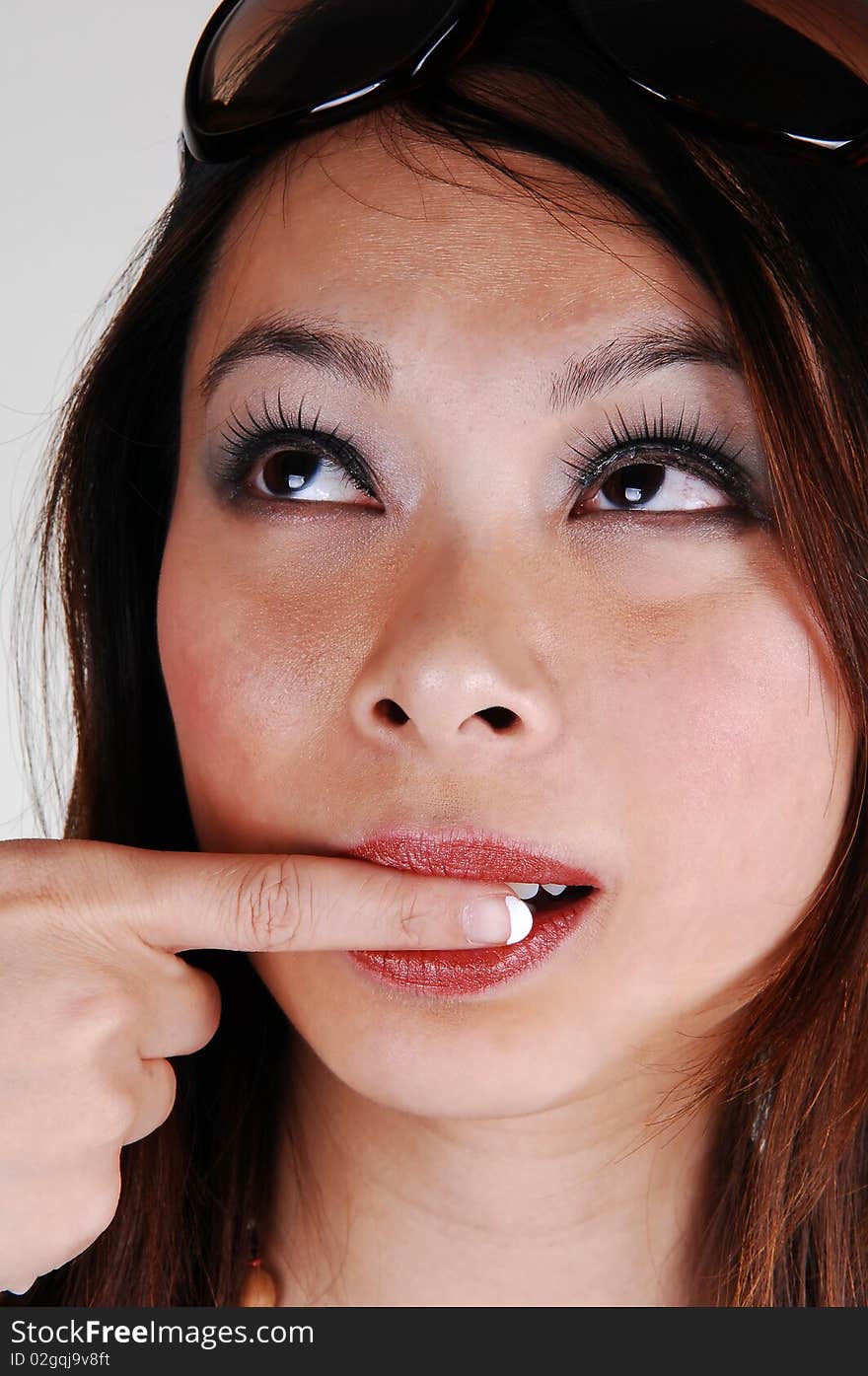 Closeup of the face of a lovely Asian woman with red lips and her finger in her mouth, with sunglasses on her forehead, for white background. Closeup of the face of a lovely Asian woman with red lips and her finger in her mouth, with sunglasses on her forehead, for white background.