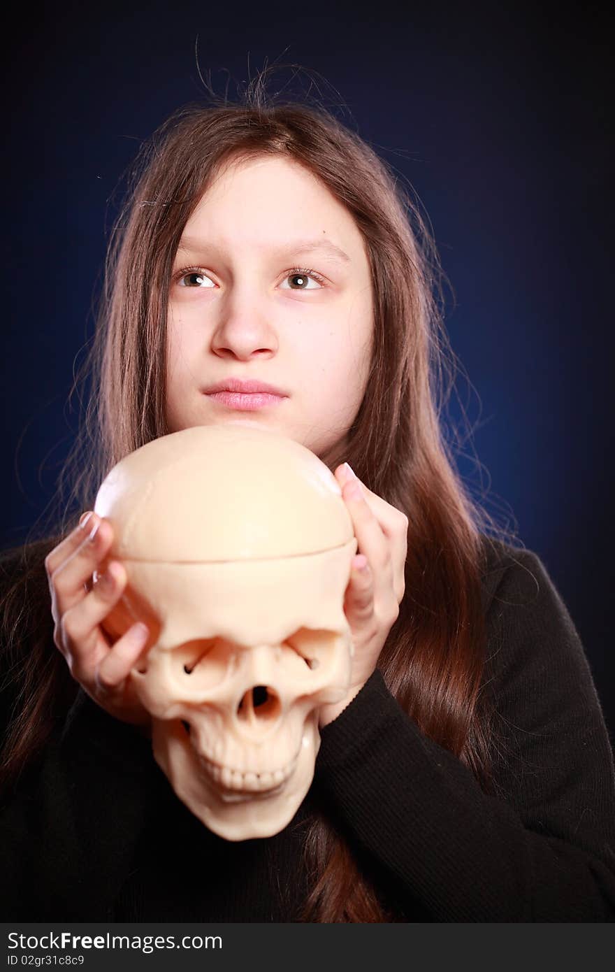 Portrait of teenager girl holding anatomical model of human skull. Black background with blue highlight. Portrait of teenager girl holding anatomical model of human skull. Black background with blue highlight