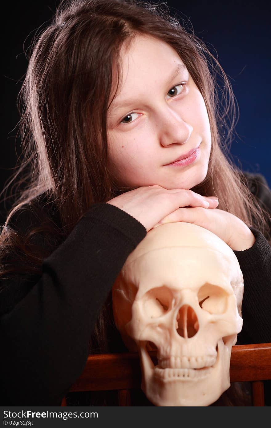 Portrait of teenager girl holding anatomical model of human skull. Black background with blue highlight. Portrait of teenager girl holding anatomical model of human skull. Black background with blue highlight