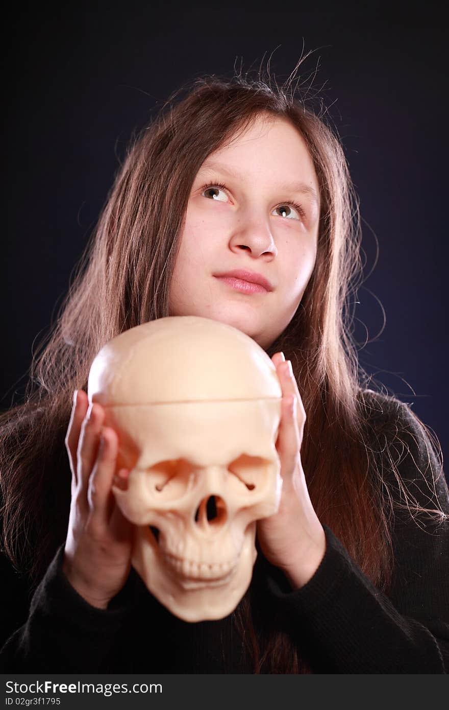 Portrait of teenager girl holding anatomical model of human skull. Black background with blue highlight. Portrait of teenager girl holding anatomical model of human skull. Black background with blue highlight