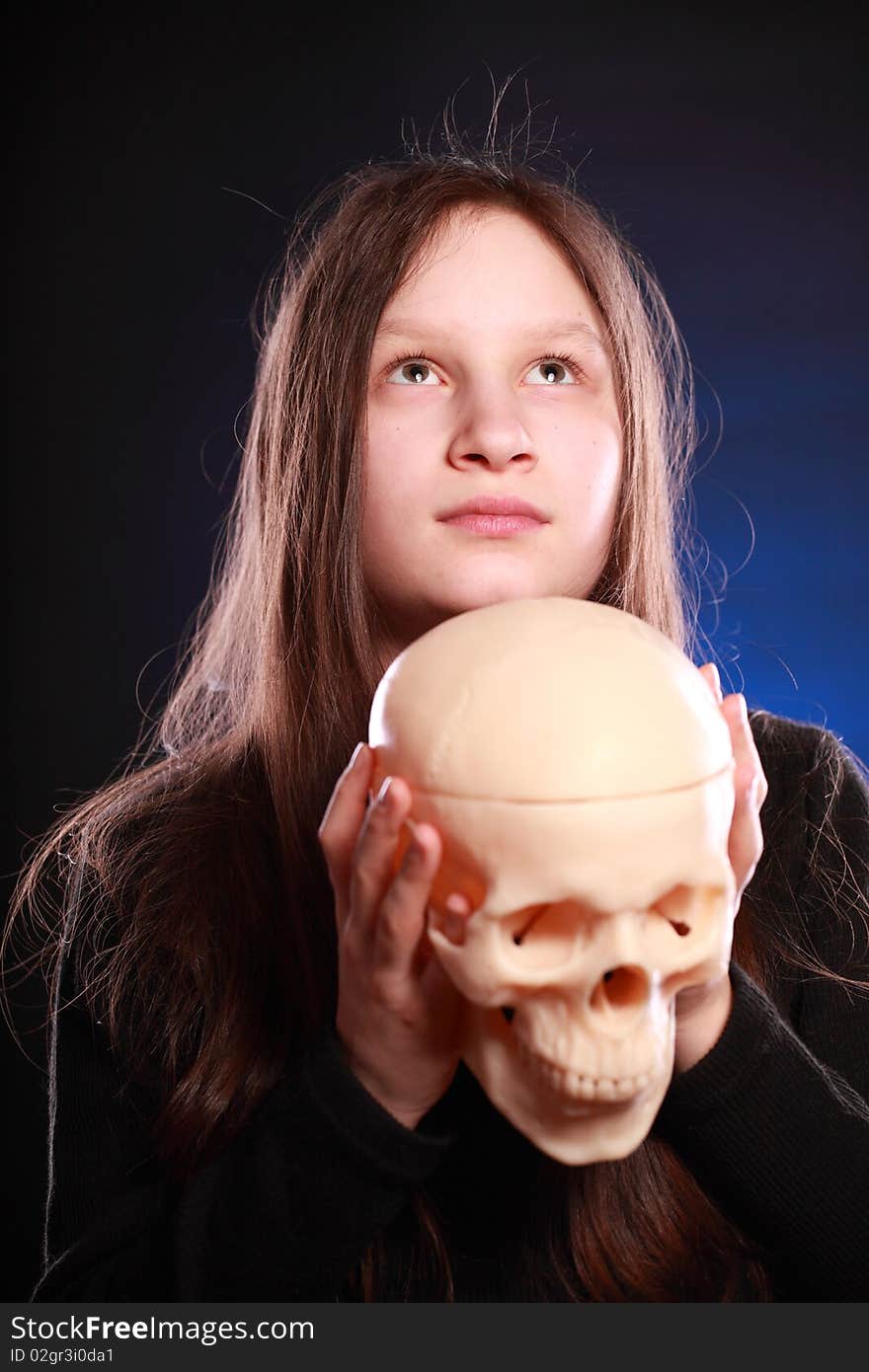 Portrait of teenager girl holding anatomical model of human skull. Black background with blue highlight. Portrait of teenager girl holding anatomical model of human skull. Black background with blue highlight