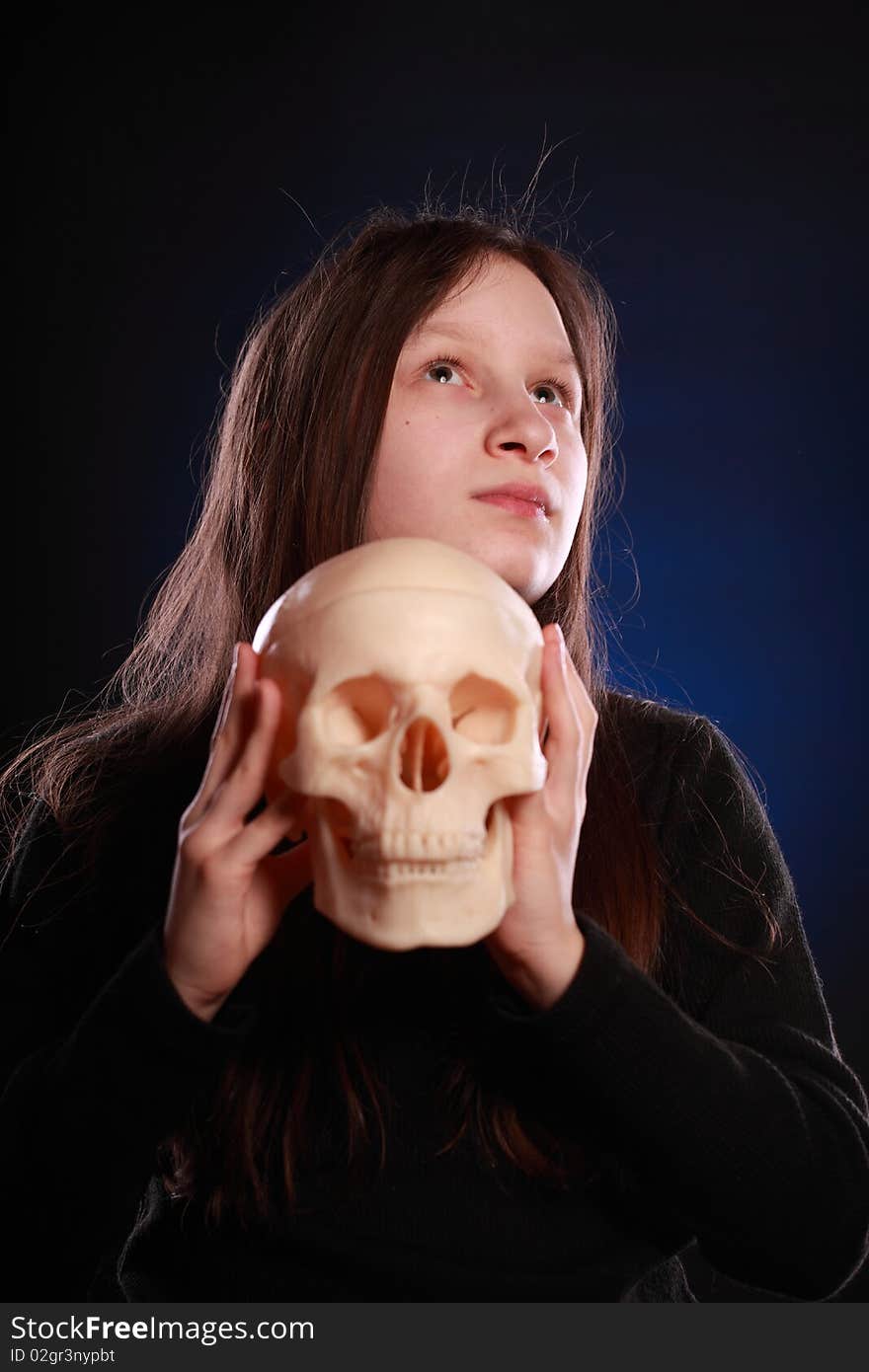 Portrait of teenager girl holding anatomical model of human skull. Black background with blue highlight. Portrait of teenager girl holding anatomical model of human skull. Black background with blue highlight