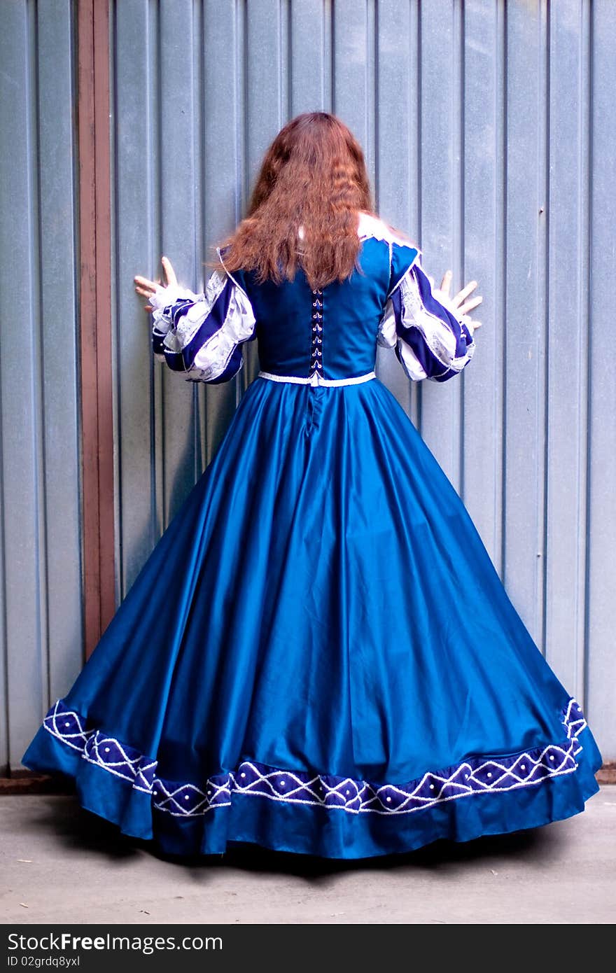 Girl in medieval blue dress standing near metal wall. Girl in medieval blue dress standing near metal wall