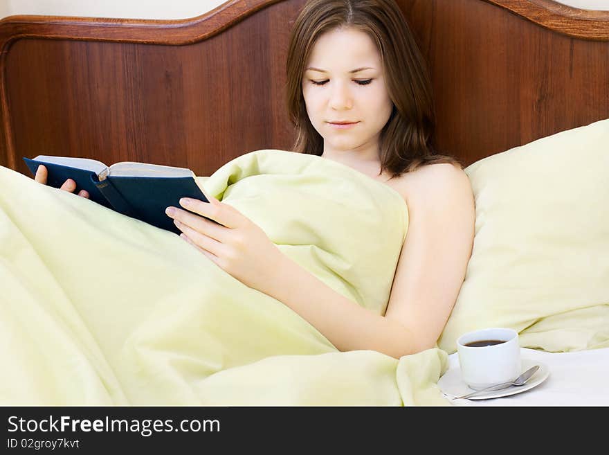 Young beautiful woman with book and cup of coffee in the bed. Young beautiful woman with book and cup of coffee in the bed