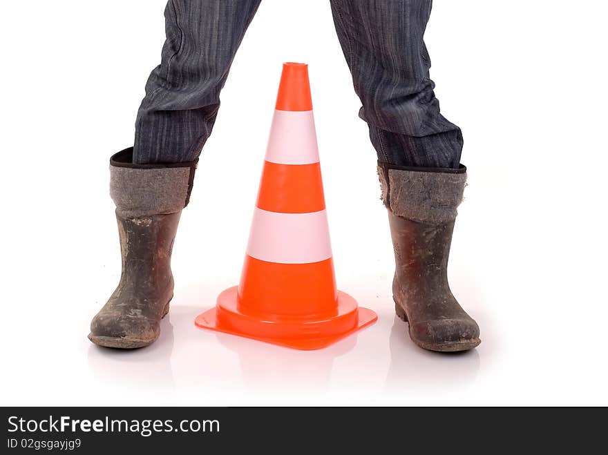 Safety cone placed between builder's legs clad in rubber boots. Safety cone placed between builder's legs clad in rubber boots.