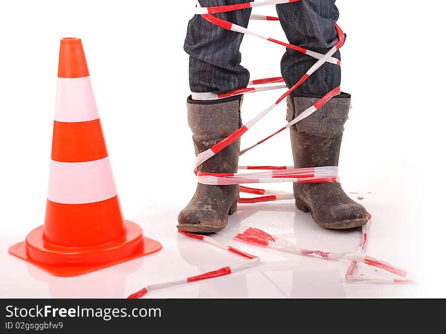 Safety cone beside worker's legs clad in rubber boots and wrapped with tape. Safety cone beside worker's legs clad in rubber boots and wrapped with tape.