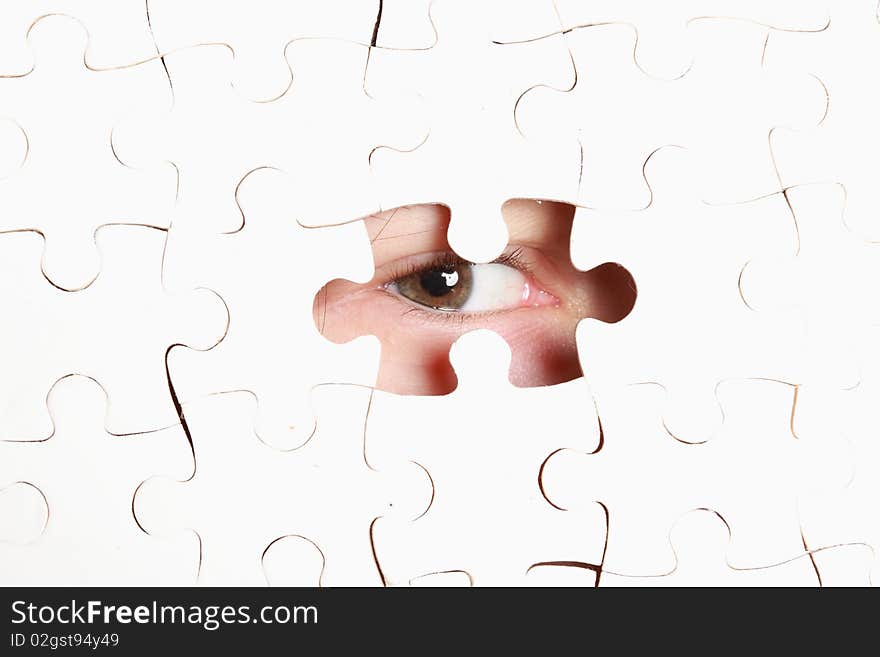 Human eye looking out through the hole in jigsaw puzzle