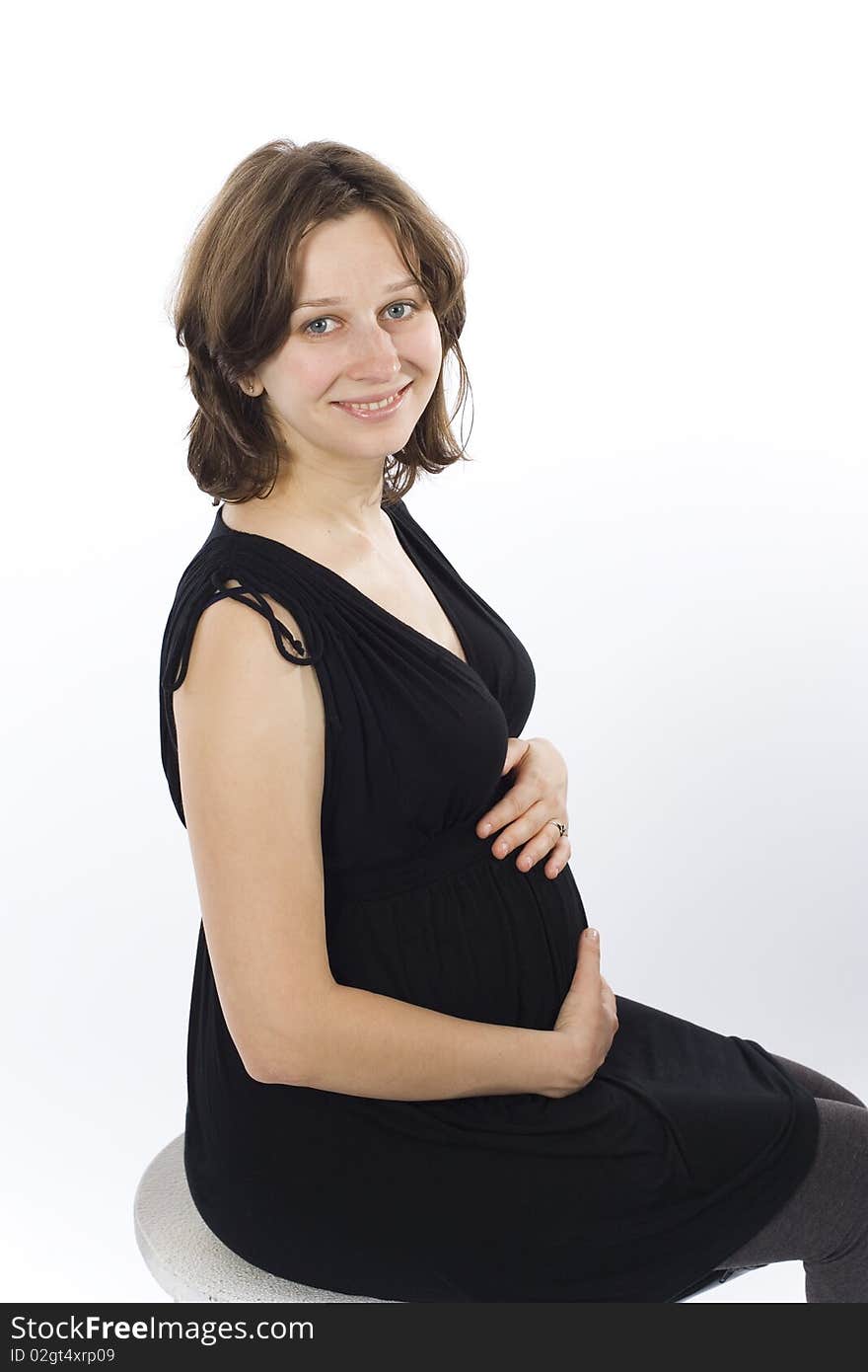 Beautiful young pregnant woman smiling and sitting in black dress on white background. Beautiful young pregnant woman smiling and sitting in black dress on white background