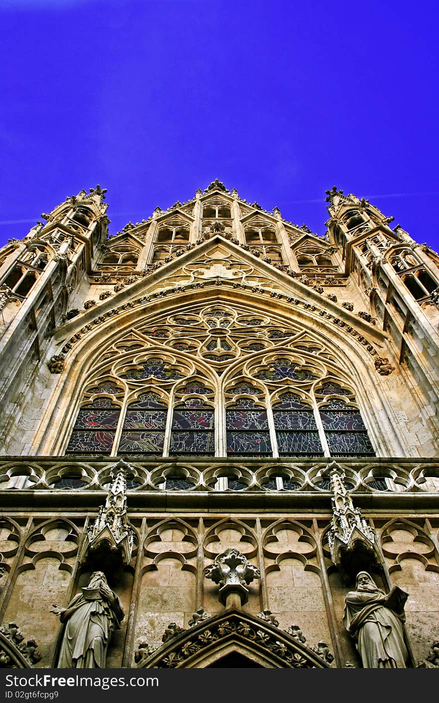 A typical Gothic Cathedral in the old medieval district of Vienna. The image shows a detail of a beautifully colored strained-glass window a trademark of the Gothic architecture. A typical Gothic Cathedral in the old medieval district of Vienna. The image shows a detail of a beautifully colored strained-glass window a trademark of the Gothic architecture.