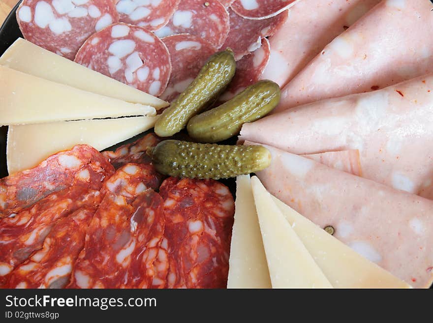 A plate of mixed salami and cheese with cucumbers. A plate of mixed salami and cheese with cucumbers