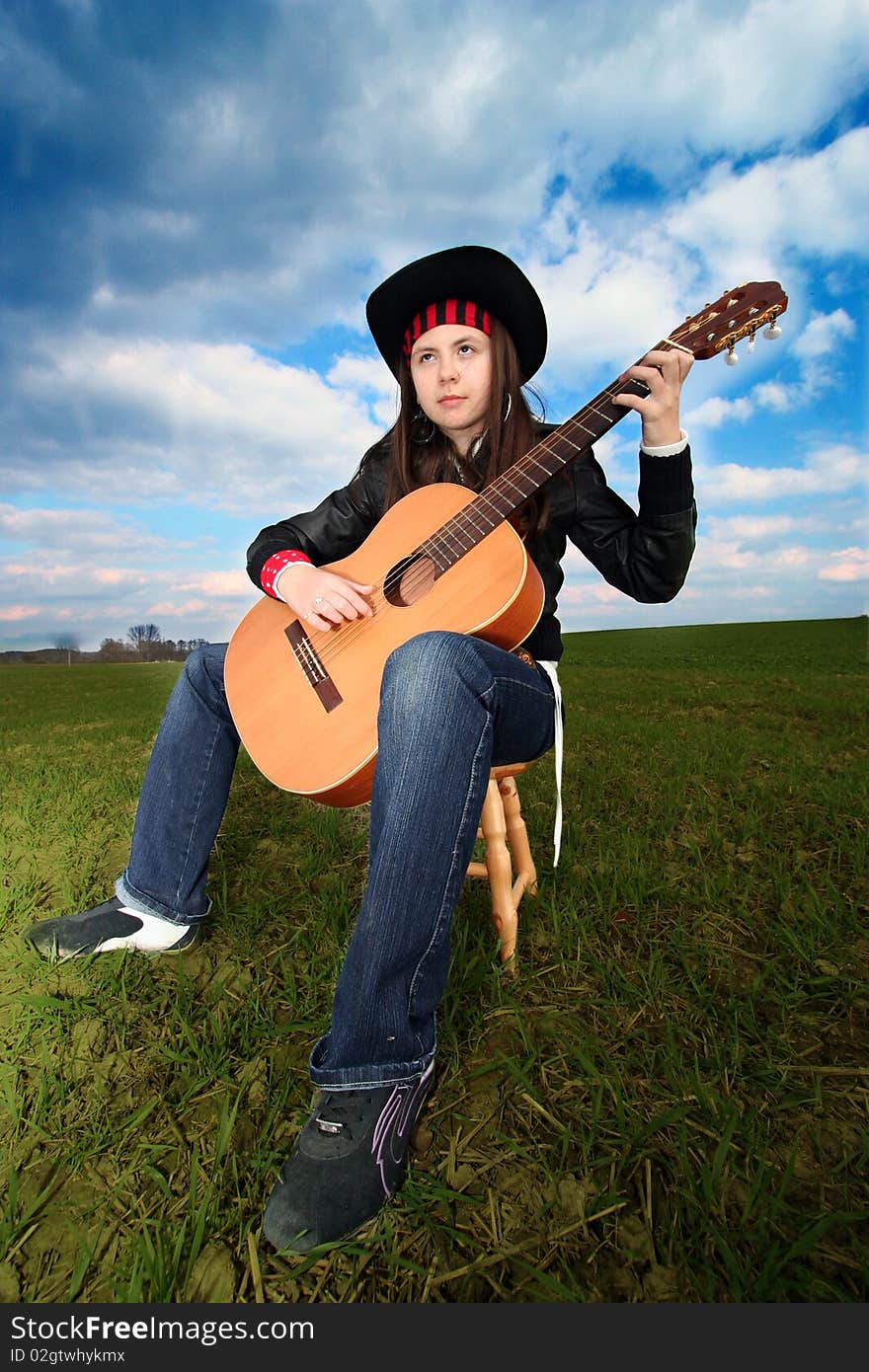 Young musican playing the guitar on the field. Young musican playing the guitar on the field