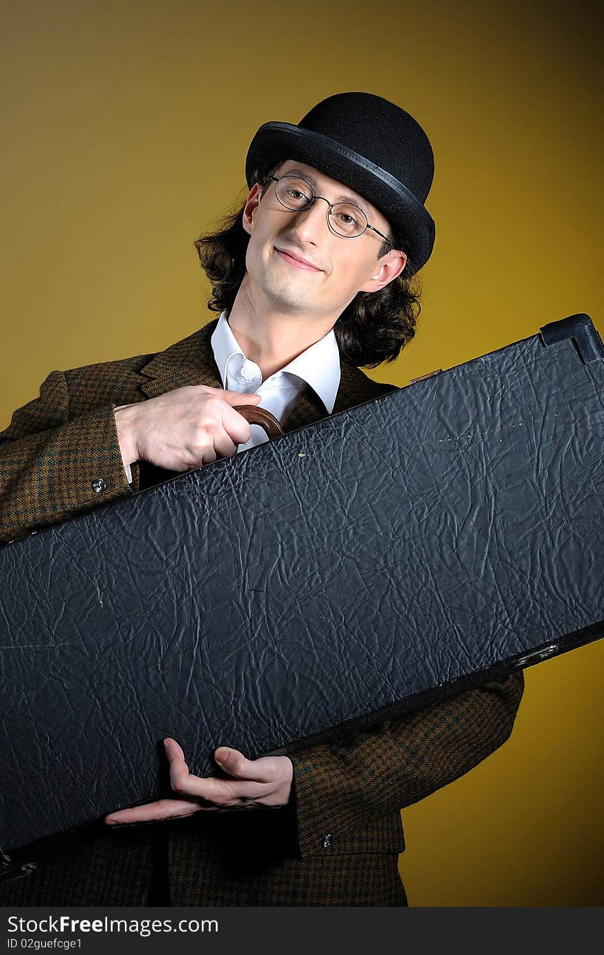 Portrait of young english retro gentleman in bowler hat holding suitcase as a luggage. yellow background. Portrait of young english retro gentleman in bowler hat holding suitcase as a luggage. yellow background