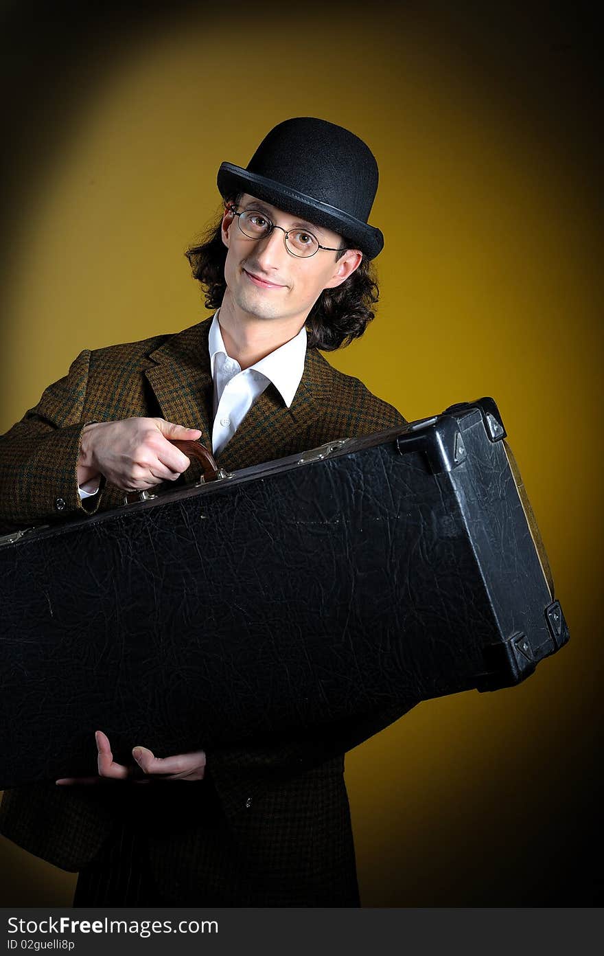 Portrait of young english retro gentleman in bowler hat holding suitcase as a luggage. yellow background. Portrait of young english retro gentleman in bowler hat holding suitcase as a luggage. yellow background