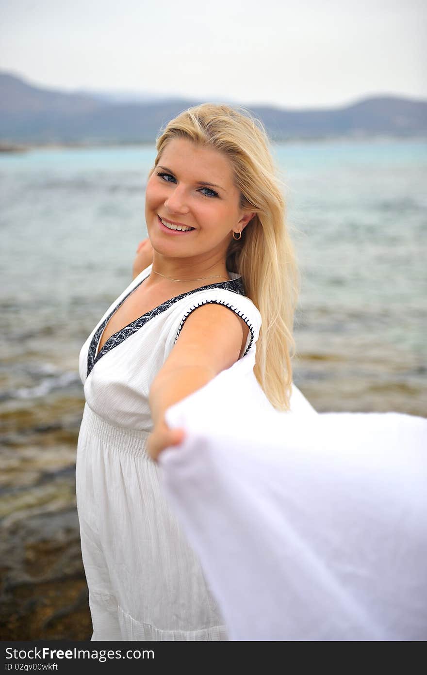 Young beautiful romantic woman in white dress dancing with shawl near blue sea