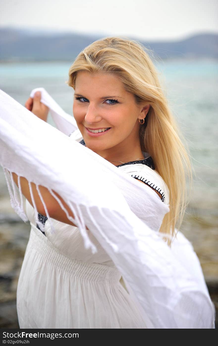 Young beautiful romantic woman in white dress dancing with shawl near blue sea