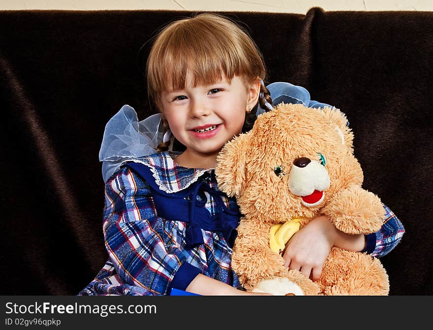 Little girl embraces bear cub sitting on sofa