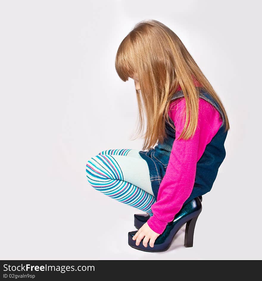 Little girl squatting in adult shoes. Little girl squatting in adult shoes